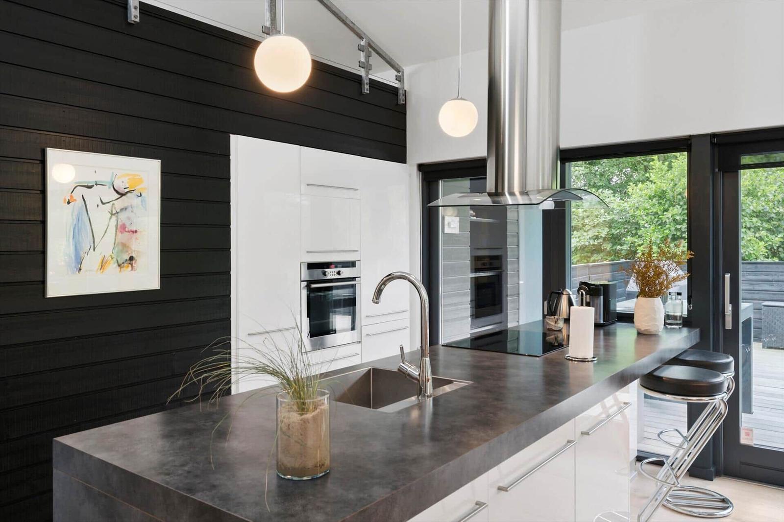 Kitchen with island, dark countertop, sink, bar stools and view of the terrace.
