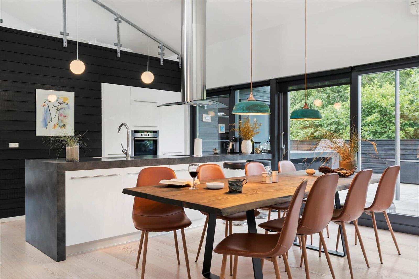 Dining area with wooden table, brown chairs and kitchen island by glass doors.