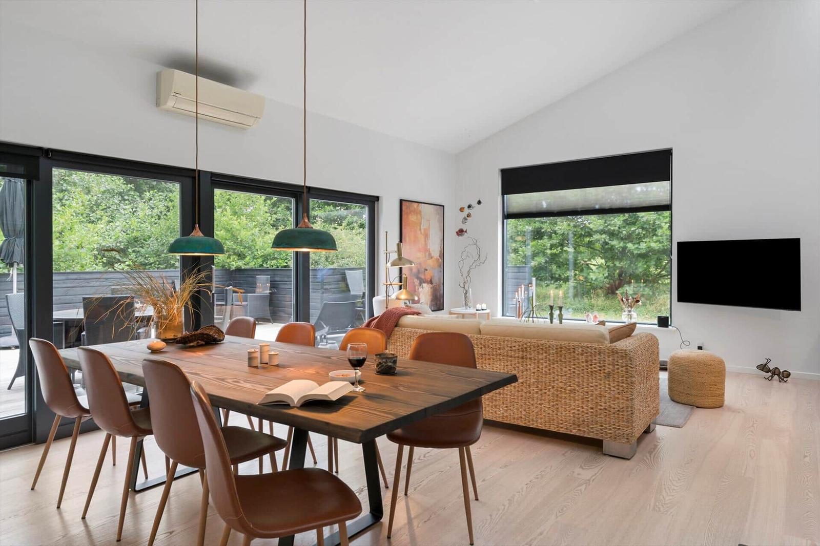 Dining table with brown chairs facing rattan sofa, TV and terrace doors.