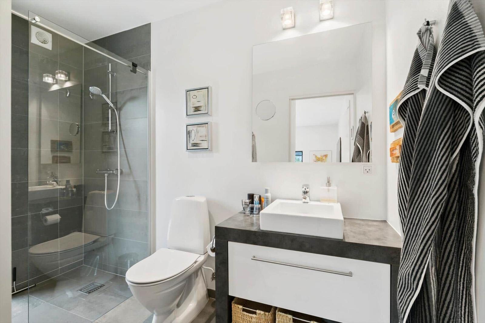 Bathroom with glass shower, toilet and washbasin on a dark counter.