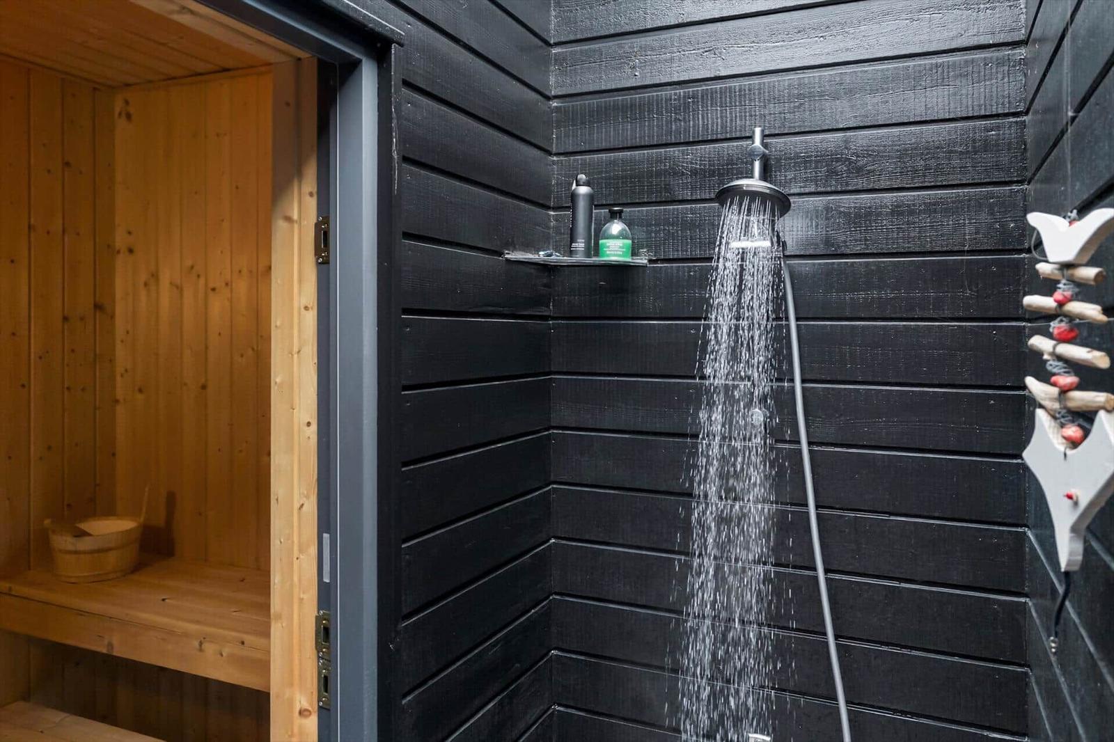 Shower with black wood cladding next to a sauna with a light wood bench.
