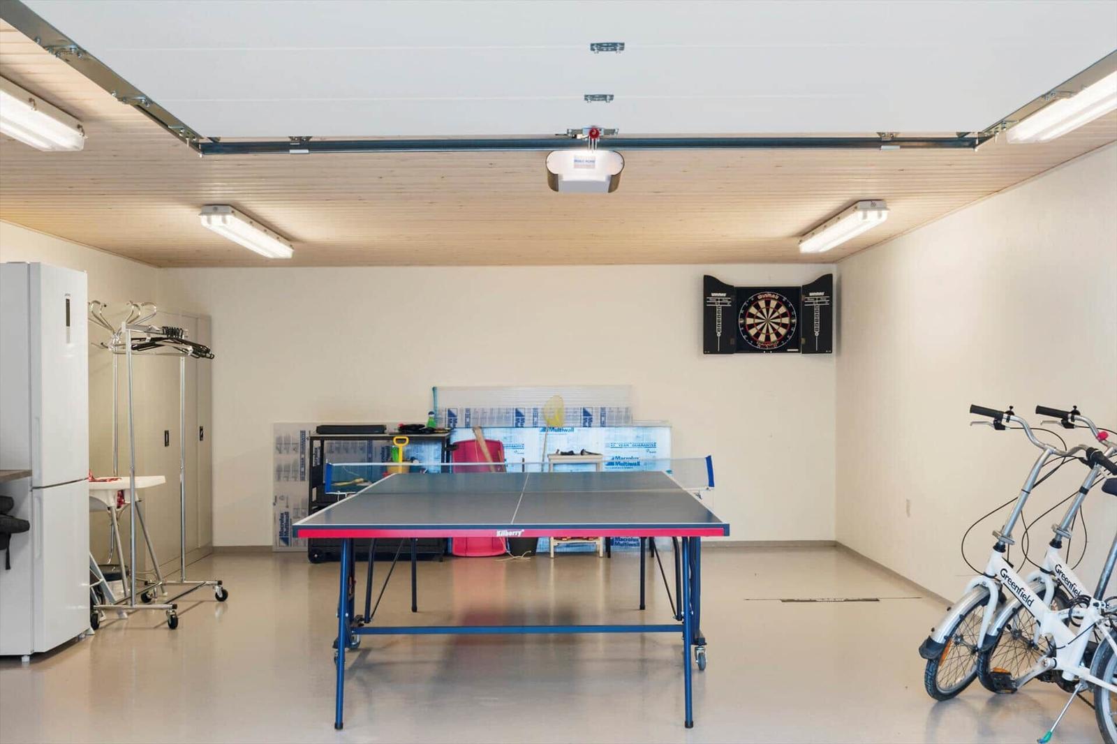 Recreation room with ping pong table, dartboard and three white bicycles.