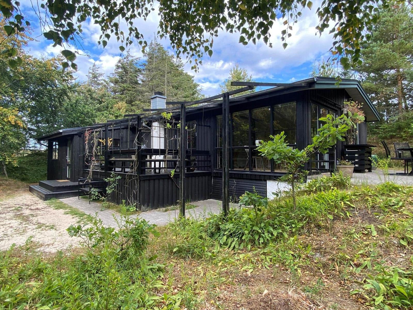 Black wooden house with terrace, railing, pergola and steps at the side door.
