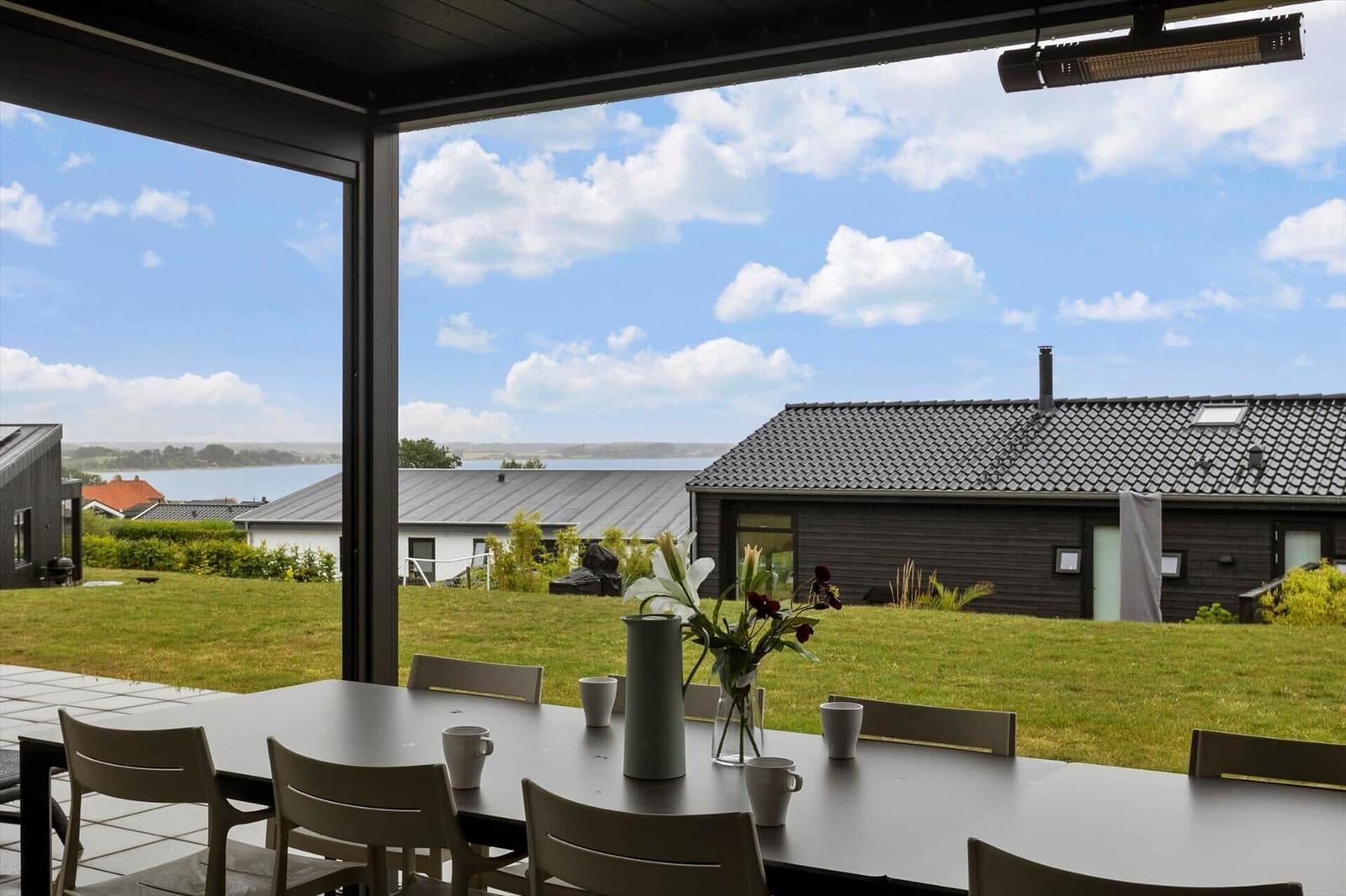 Covered terrace with dining table, lawn and view of the water.