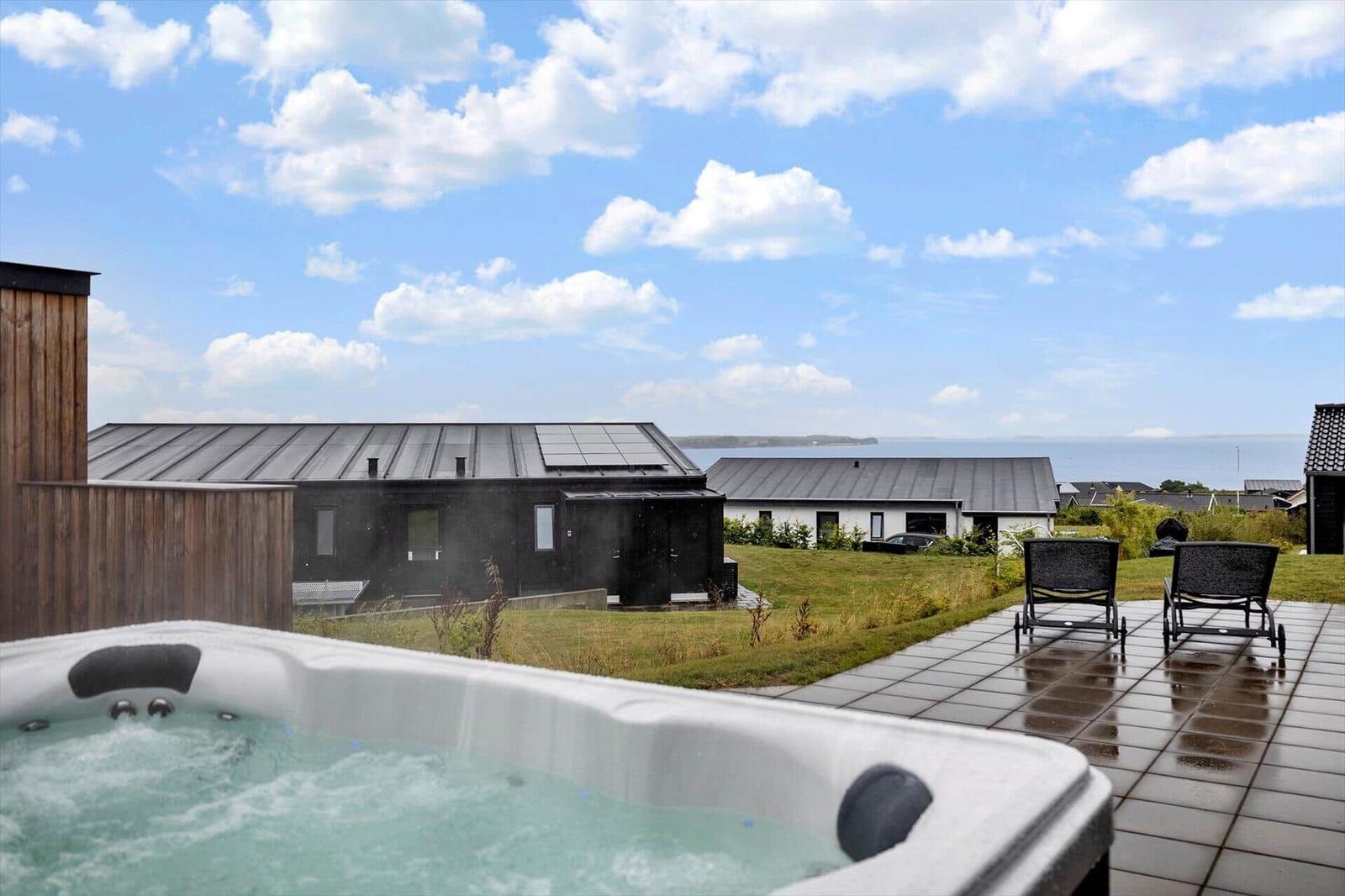 Bubbling outdoor hot tub on terrace with loungers and water view.