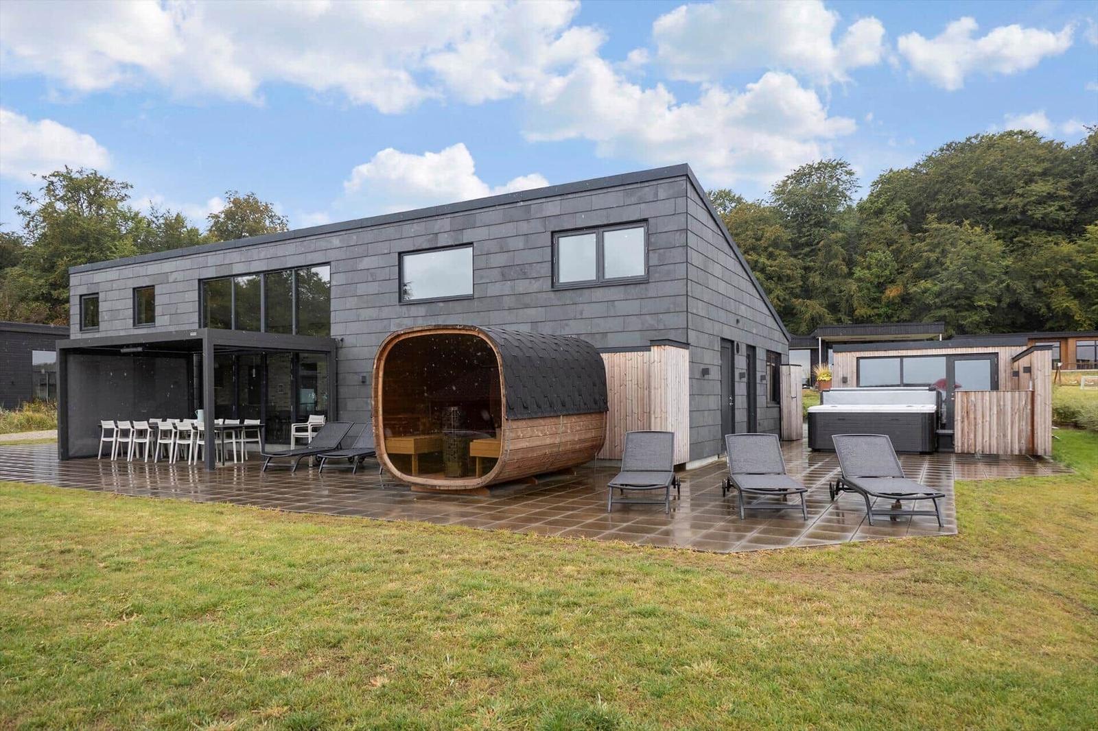 House with terrace, barrel sauna, hot tub and sun loungers by the lawn.