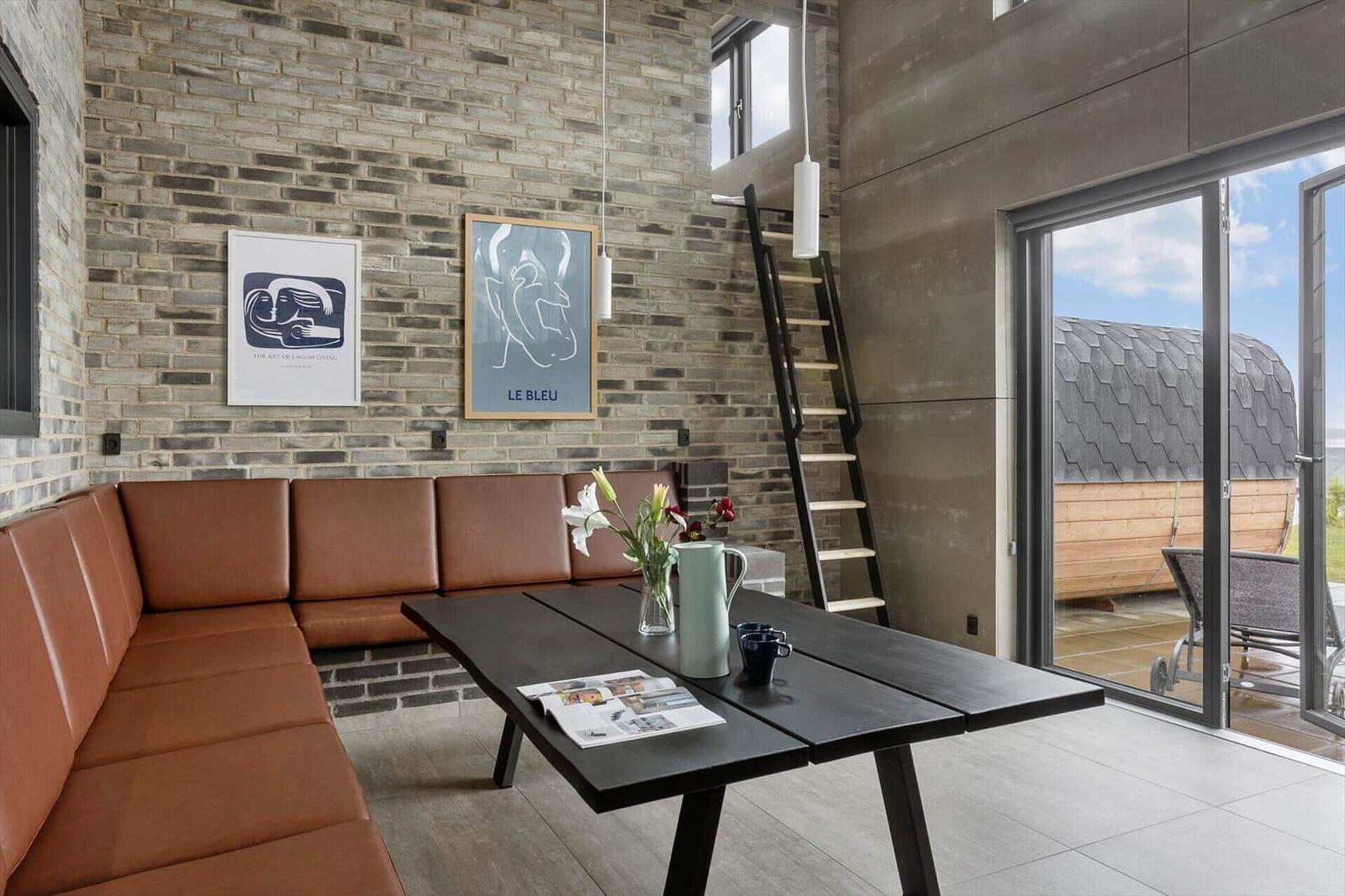 Leather corner bench at dining table, brick wall and barrel sauna view.
