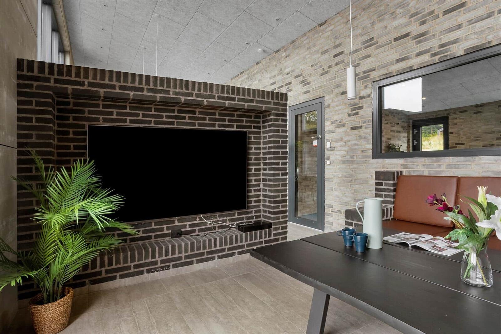 Living nook with TV in brick wall, palm plant and brown leather bench.