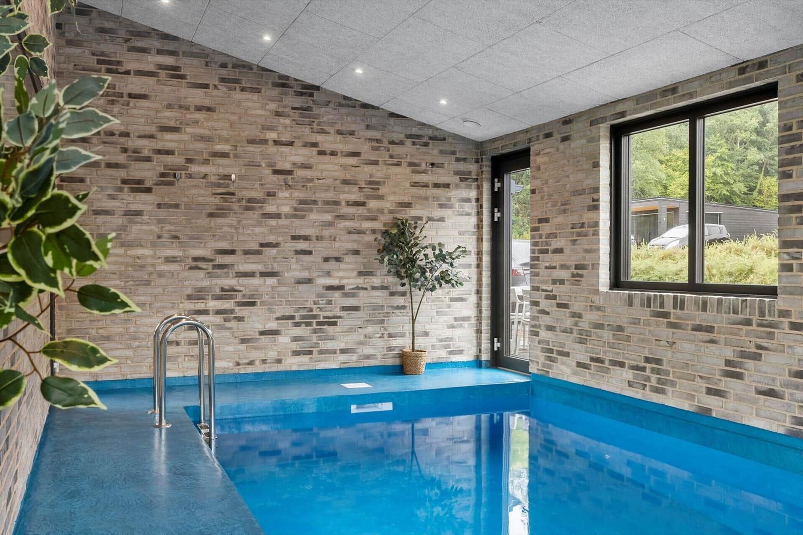 Indoor pool with entry ladder, brick walls and glass door to outside.