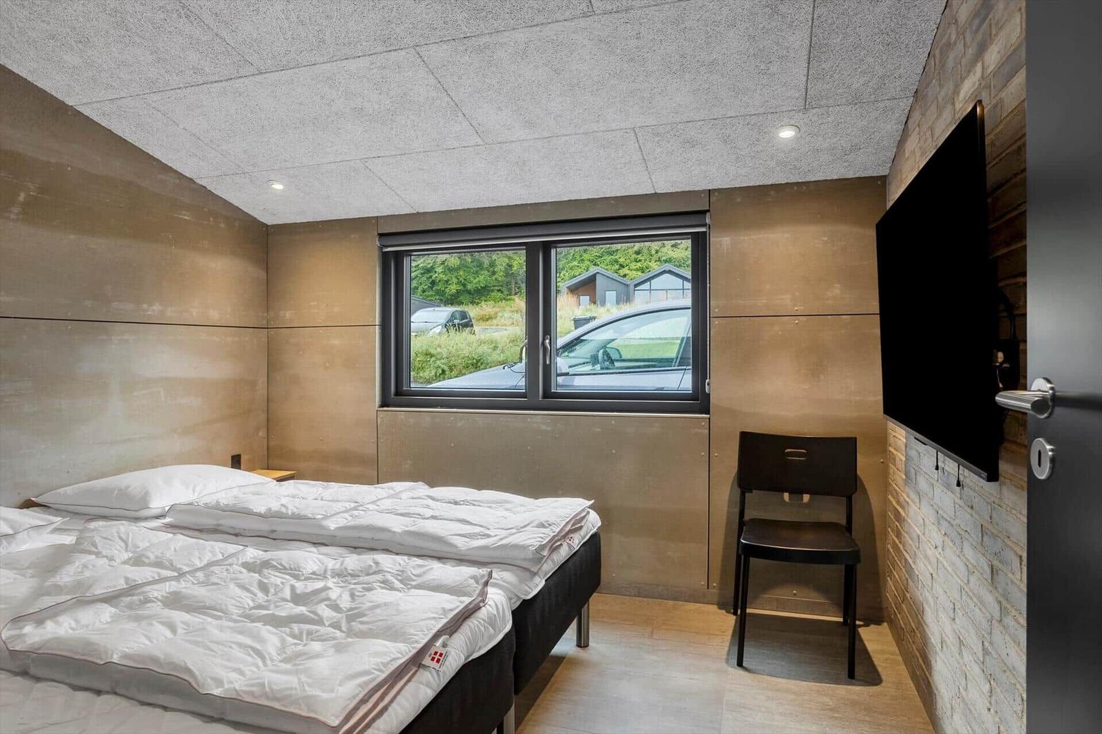 Bedroom with two white single beds, TV on a brick wall and a black chair.