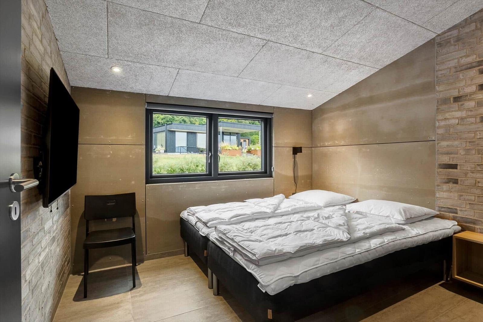 Bedroom with two beds, black wall lamp, nightstand and TV on brick wall.