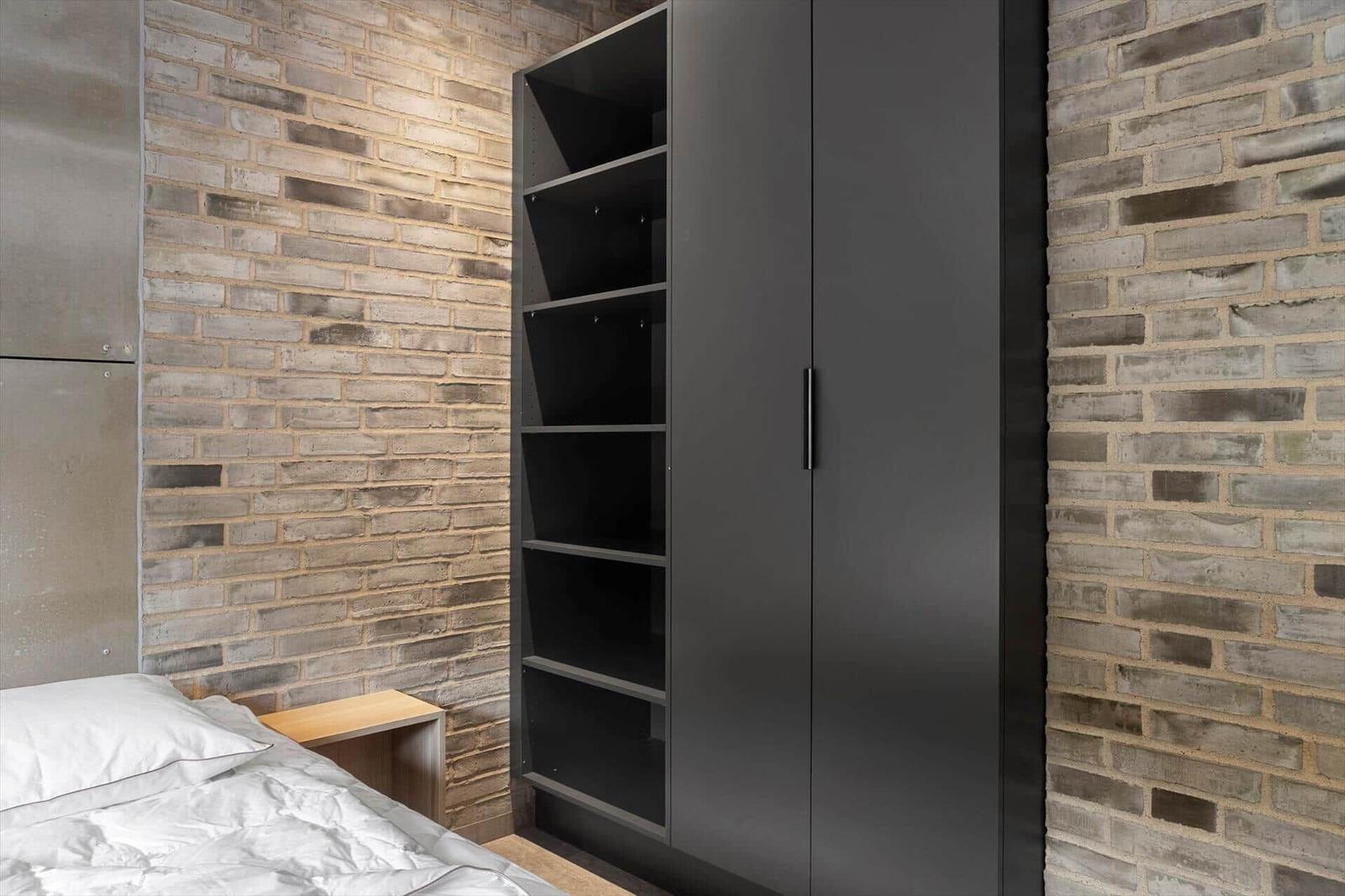 Tall black wardrobe with open shelves and doors against a brick wall.
