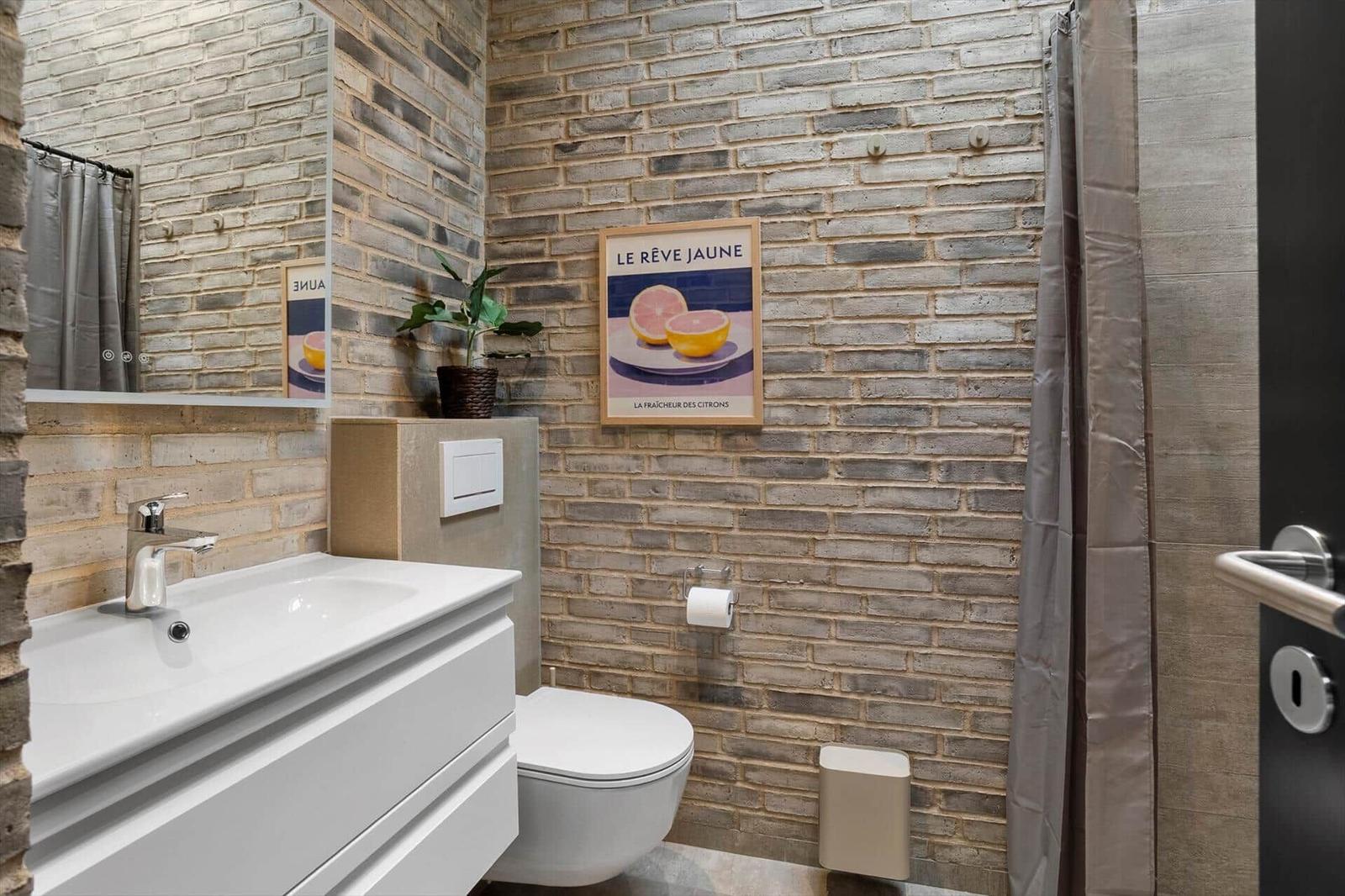 Bathroom with vanity, wall-hung toilet, potted plant and shower curtain.