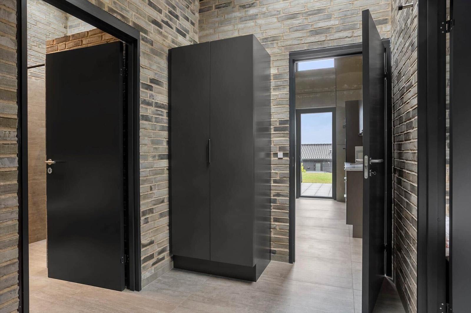 Hallway with brick walls, black wardrobe and view to a glass door outside.