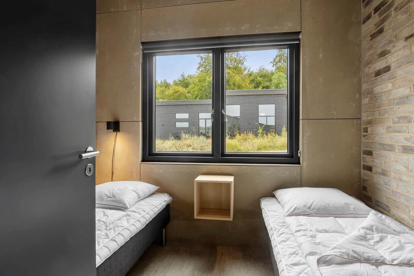 Bedroom with two single beds, a window between them and a wooden shelf.