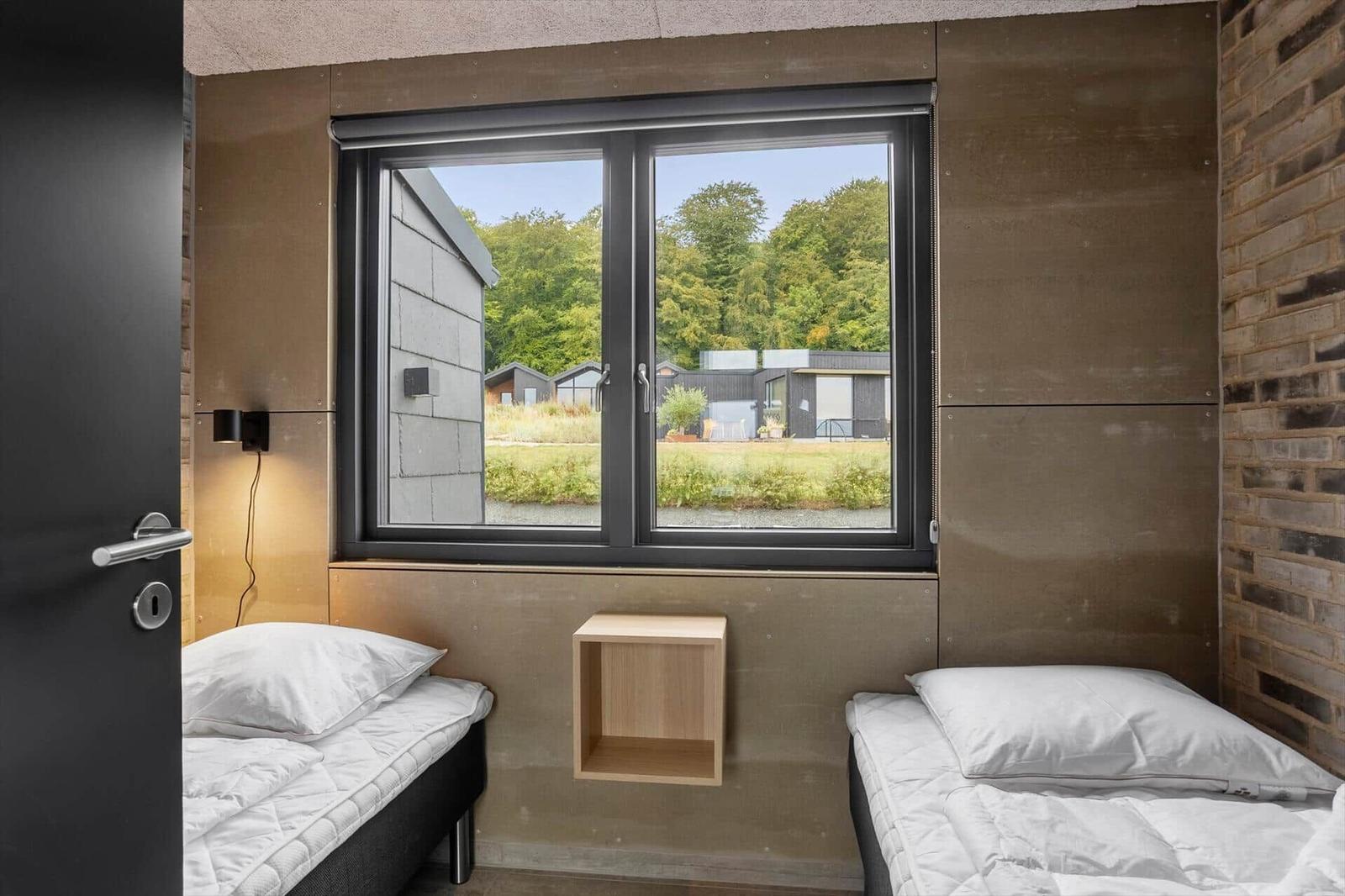 Bedroom with two single beds under the window, wall lamp and brick wall.