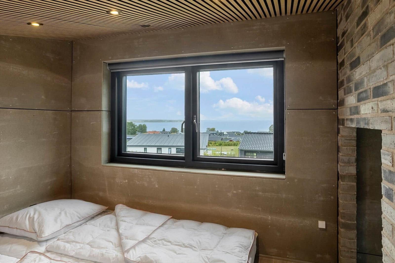 Bedroom with window view of rooftops and water, wood slat ceiling and bed.