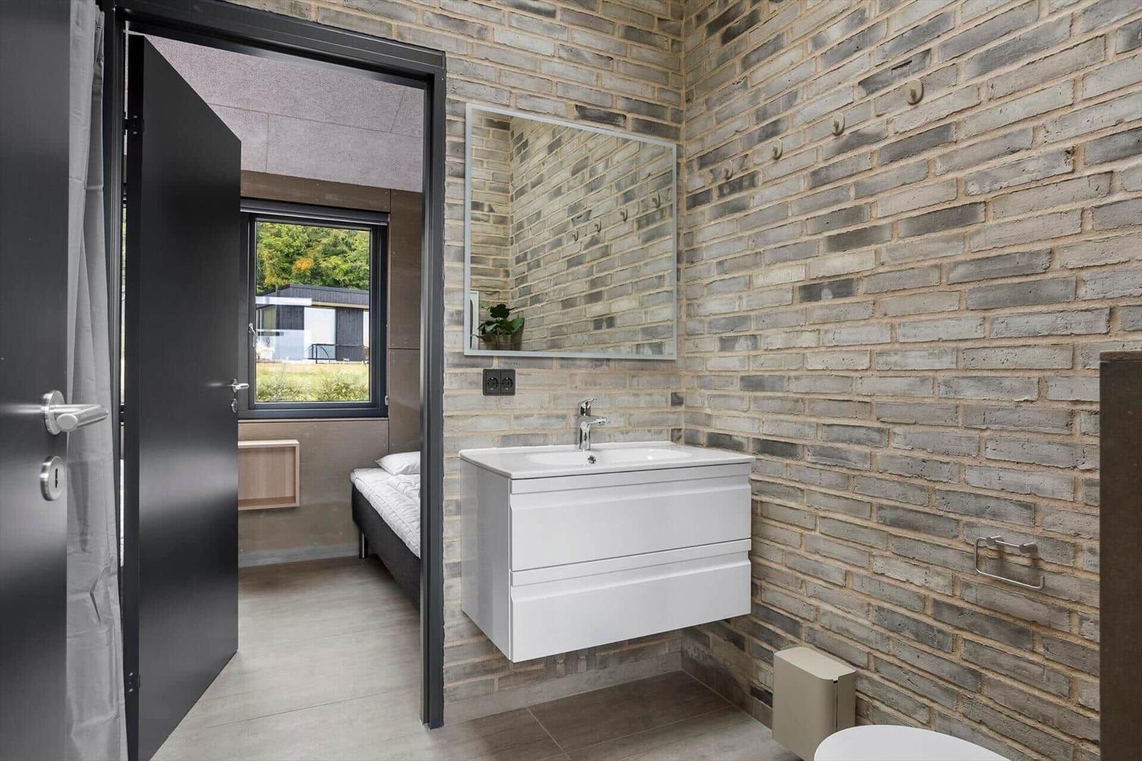 Bathroom with white vanity on brick wall and open door to the bedroom.