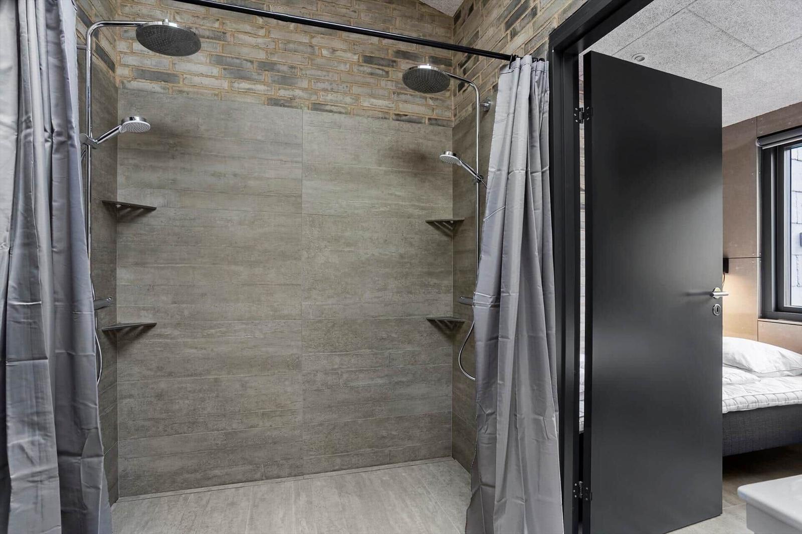 Bathroom with two walk-in showers, handheld sprays, grey tiles and curtains.