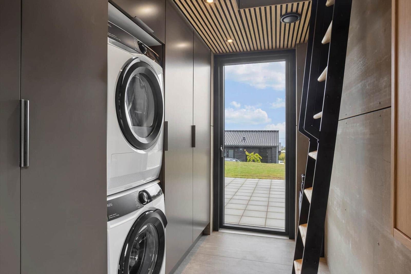 Hallway with washer and dryer in cabinets, a ladder and a glass door.