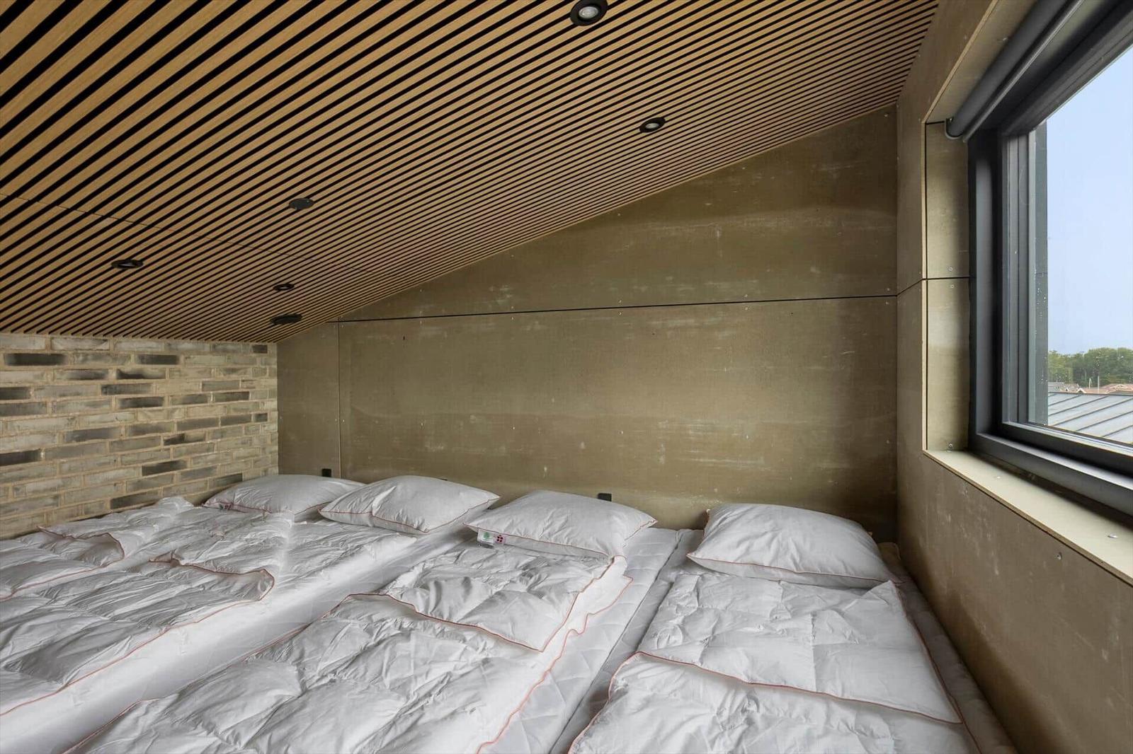Sleeping area under sloped wood slat ceiling with three floor beds and a brick wall.