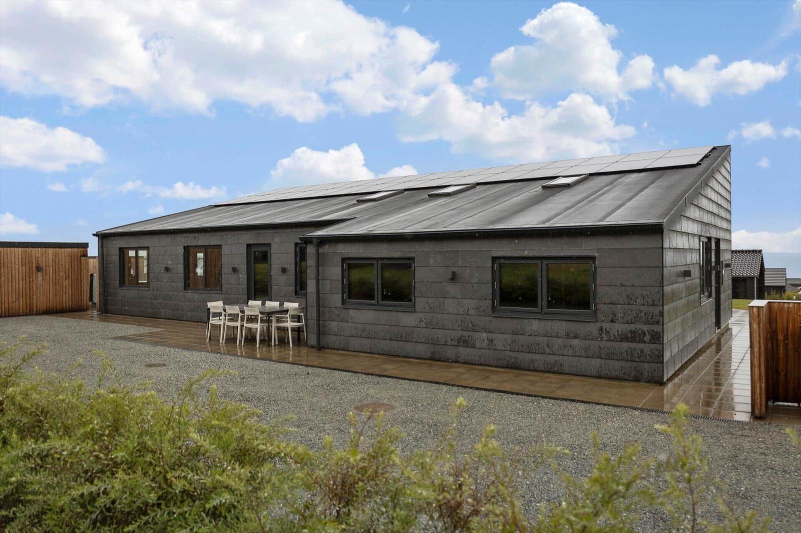 Dark house with slate facade, terrace, dining table and white chairs.