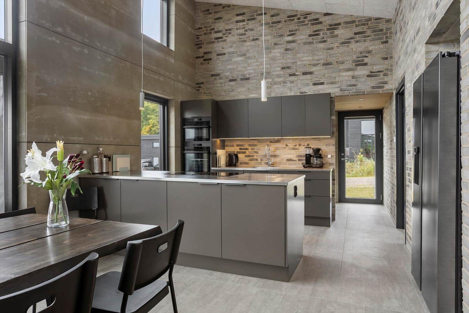 Dark kitchen with island, brick wall, oven and dining table.
