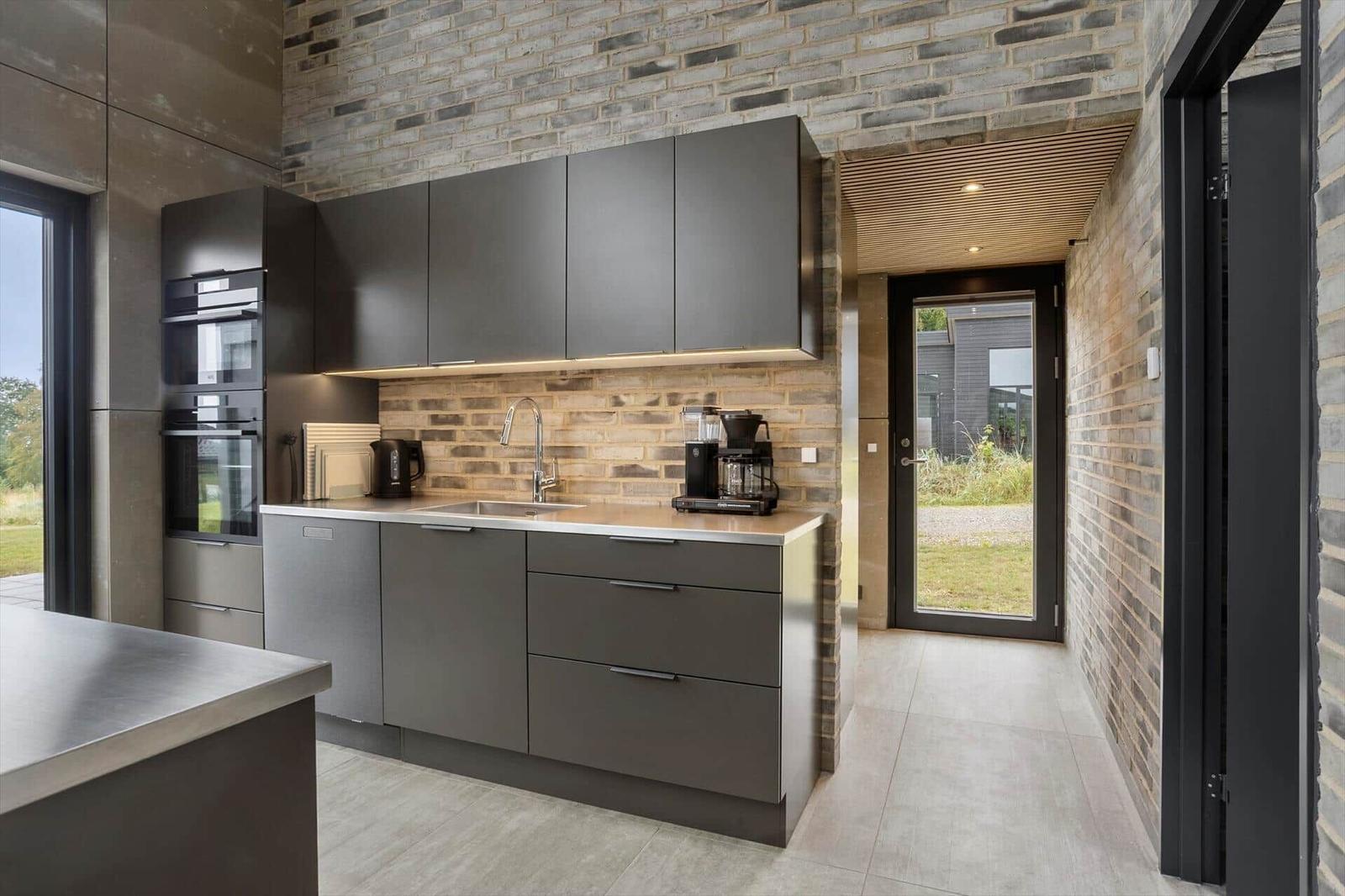 Anthracite kitchen units with oven, sink and exposed brick wall.