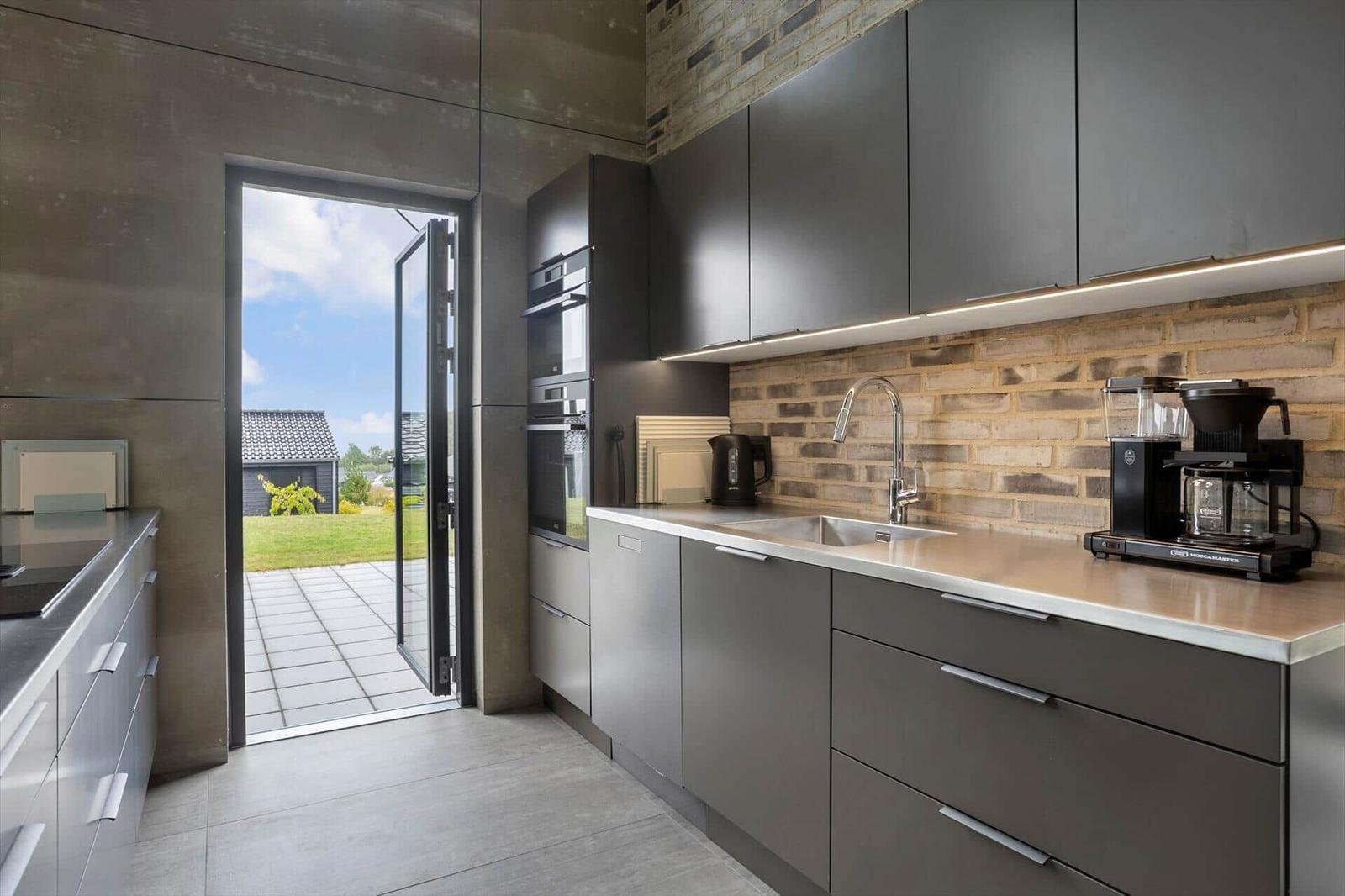 Dark kitchen with brick wall, stainless sink and open terrace door.