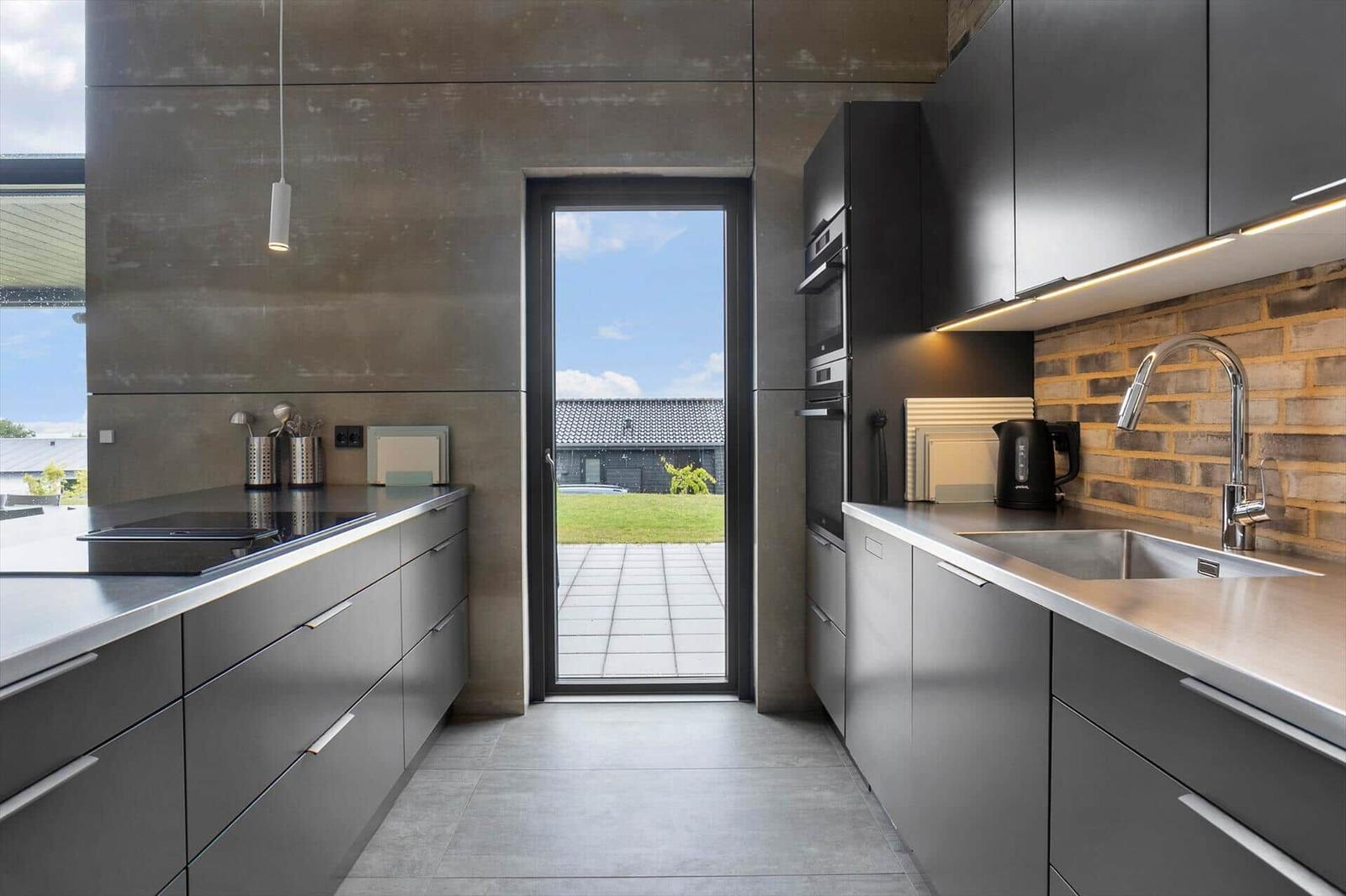Galley kitchen with stainless steel, hob and glass door to outside.