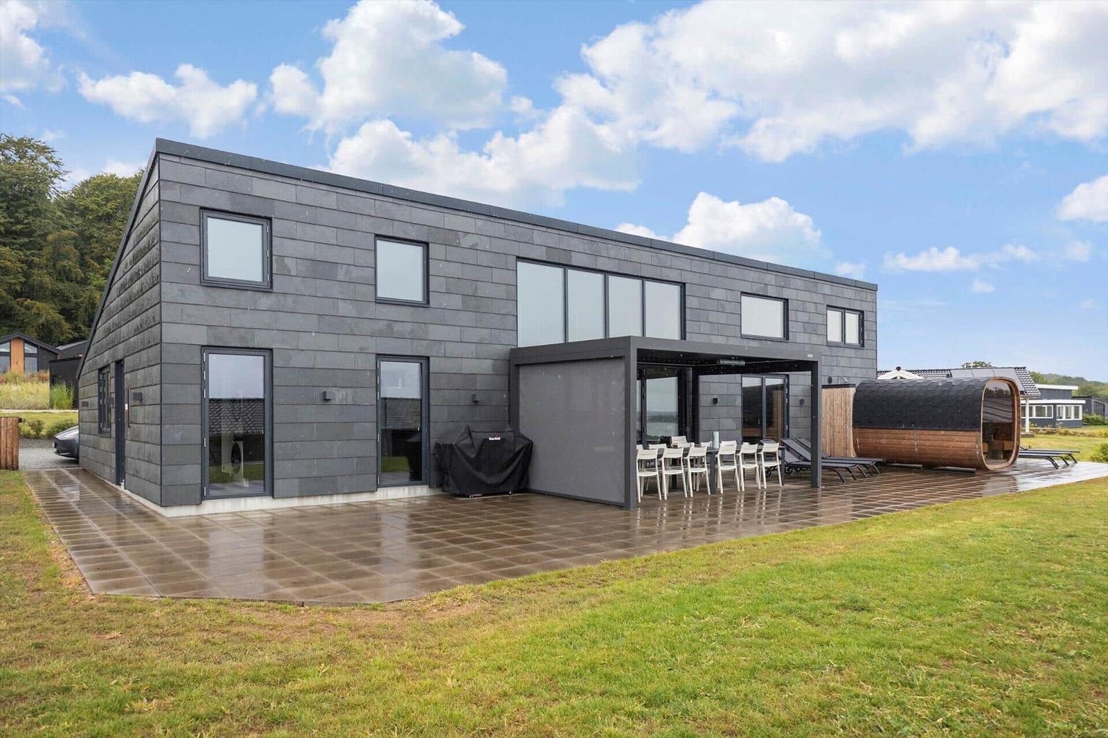Dark house with terrace, dining table, barrel sauna and sun loungers.