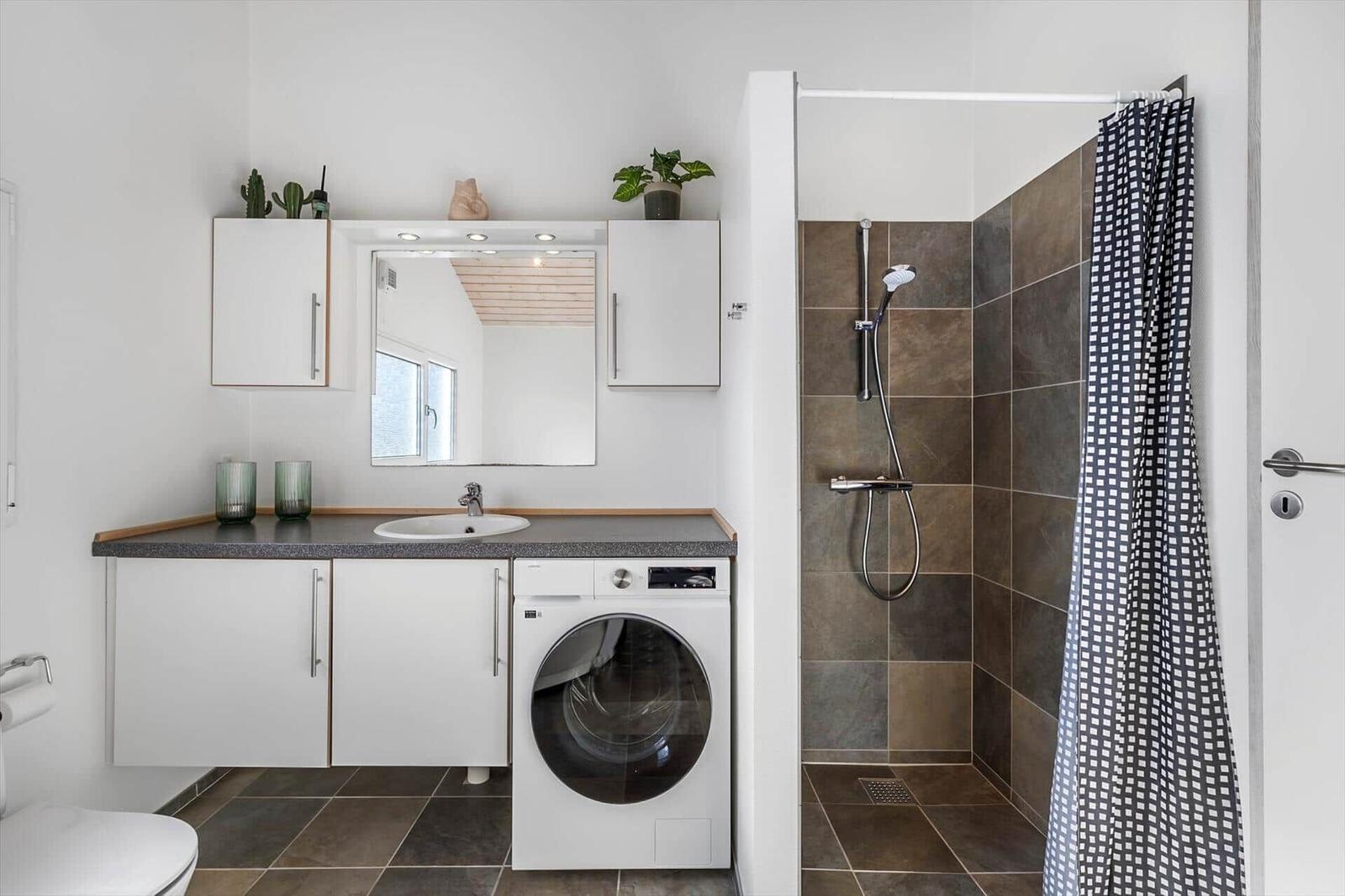 Bathroom with vanity, washing machine and tiled shower with a checked curtain.
