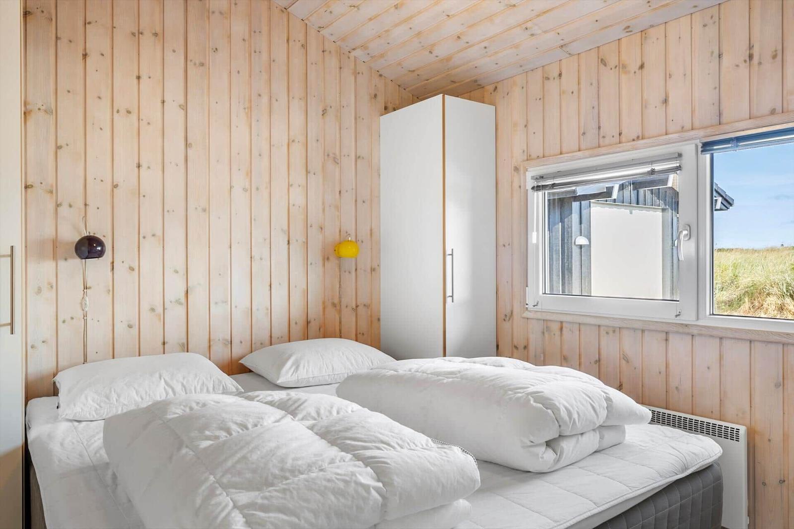 Bedroom with wood walls, double bed, white wardrobe and a window to the dunes.