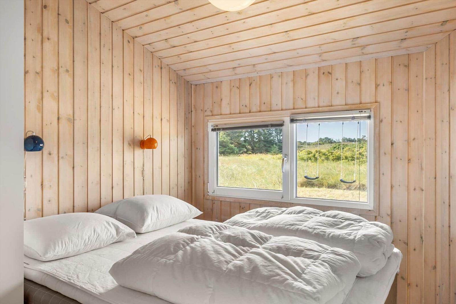 Bedroom with wood walls, double bed and window view of a meadow with swings.