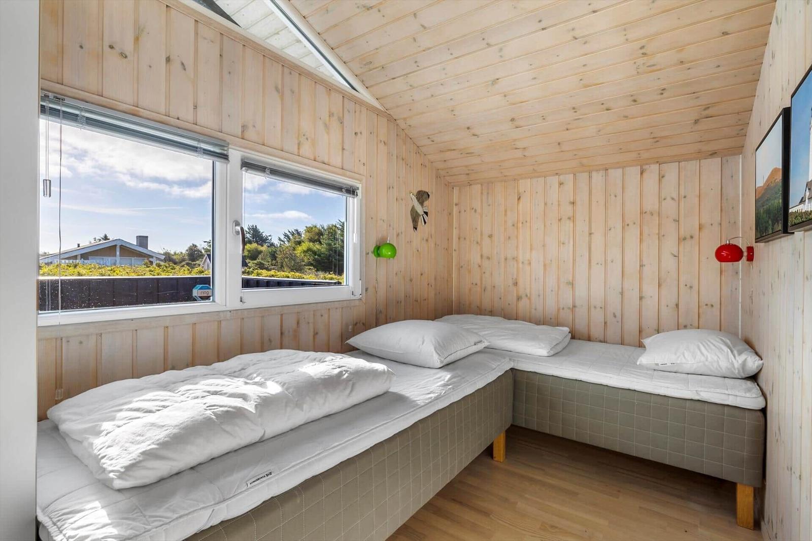 Bedroom with two single beds in an L-shape, wood paneling and a small skylight.