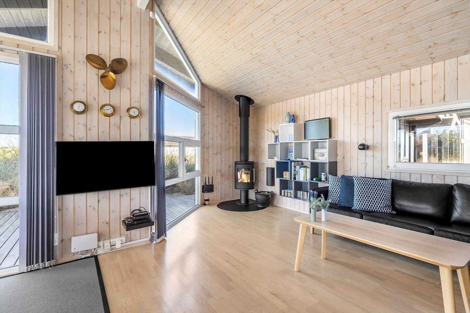 Living room with leather sofa, coffee table, wood stove and TV on light wood walls.