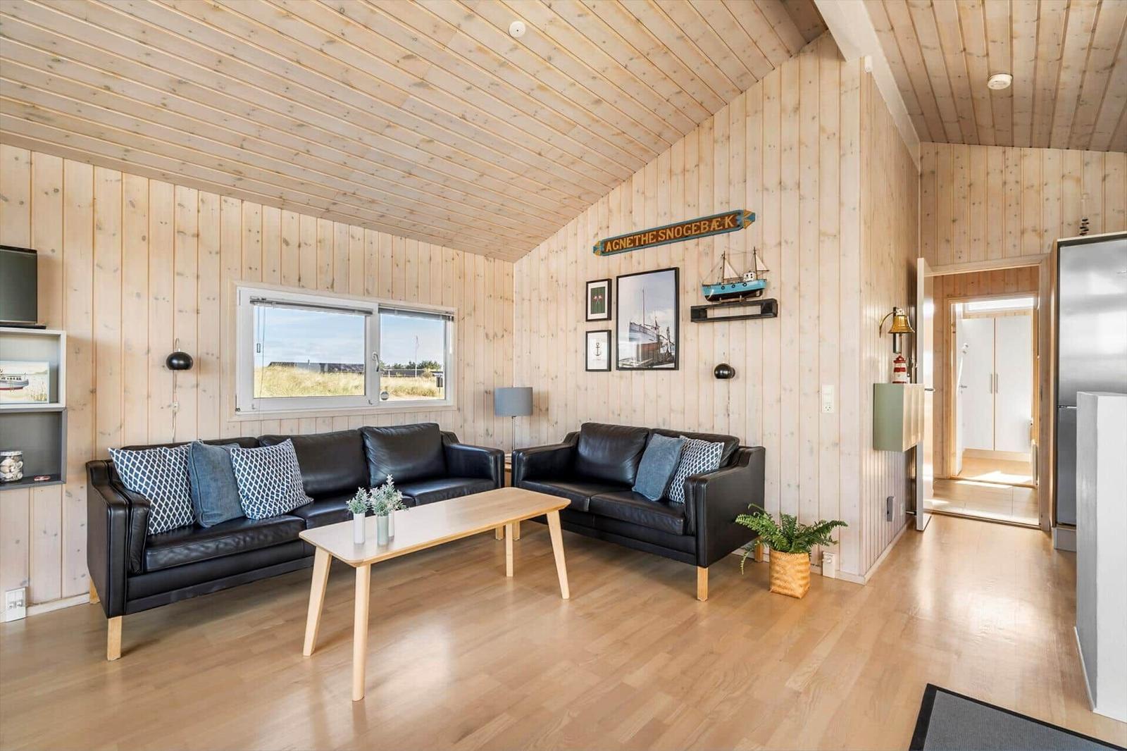 Living area with two leather sofas, light coffee table and nautical decor on wood walls.
