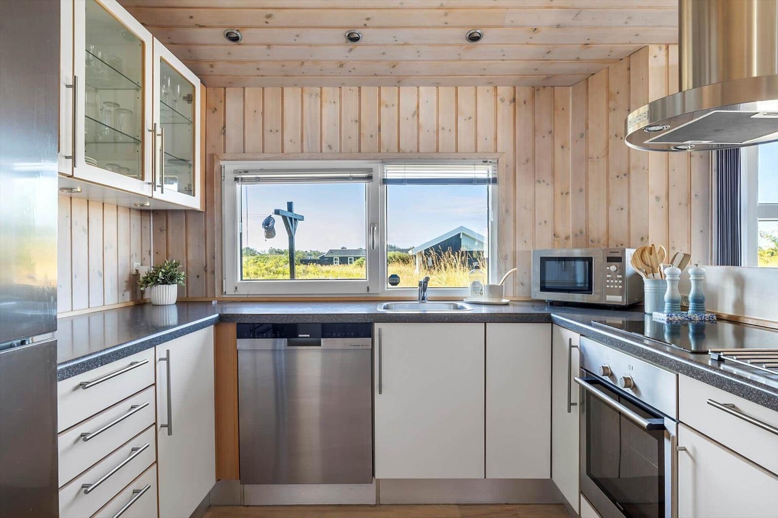 U-shaped kitchen with white cabinets, steel appliances and a window onto greenery.