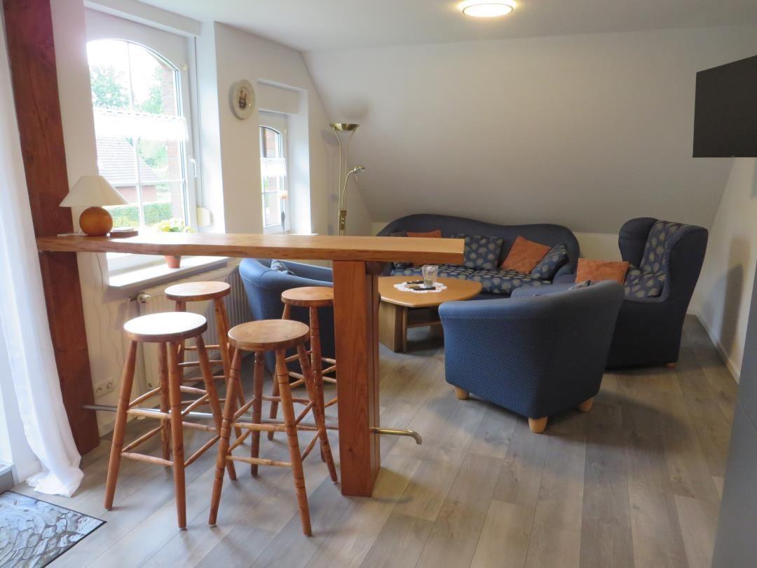 Wohnbereich mit Holztresen, vier Barhockern und blauer Sofaecke unter Dachschräge.