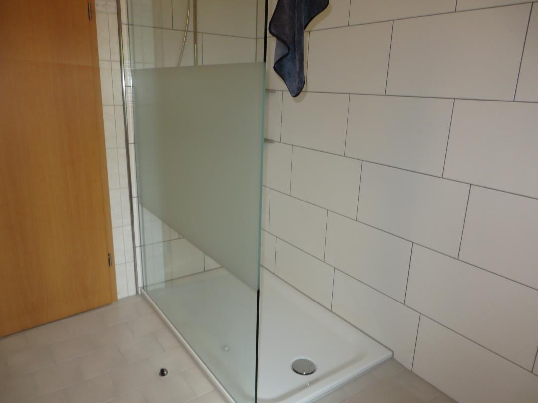 Begehbare Dusche mit Glaswand, Milchglasstreifen und weißer Duschwanne.