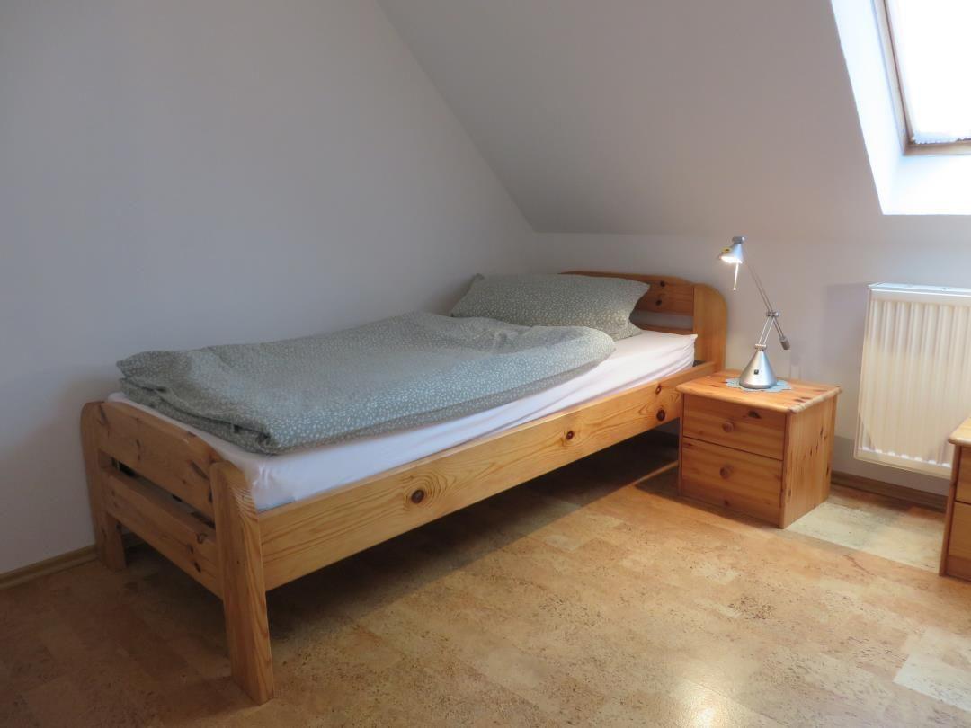 Einzelbett aus Holz mit Nachttisch, Leselampe und Heizkörper unter Dachfenster.