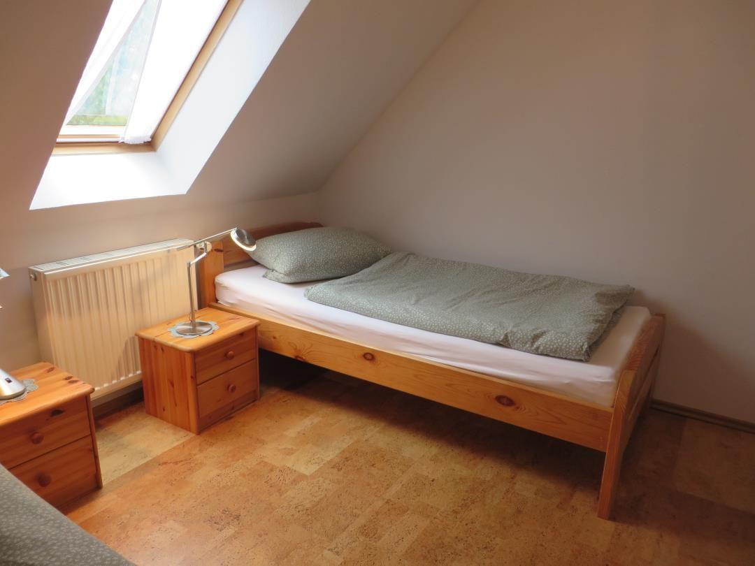 Holzbett mit grüner Bettwäsche, Nachttisch und Leselampe unter Dachschräge.