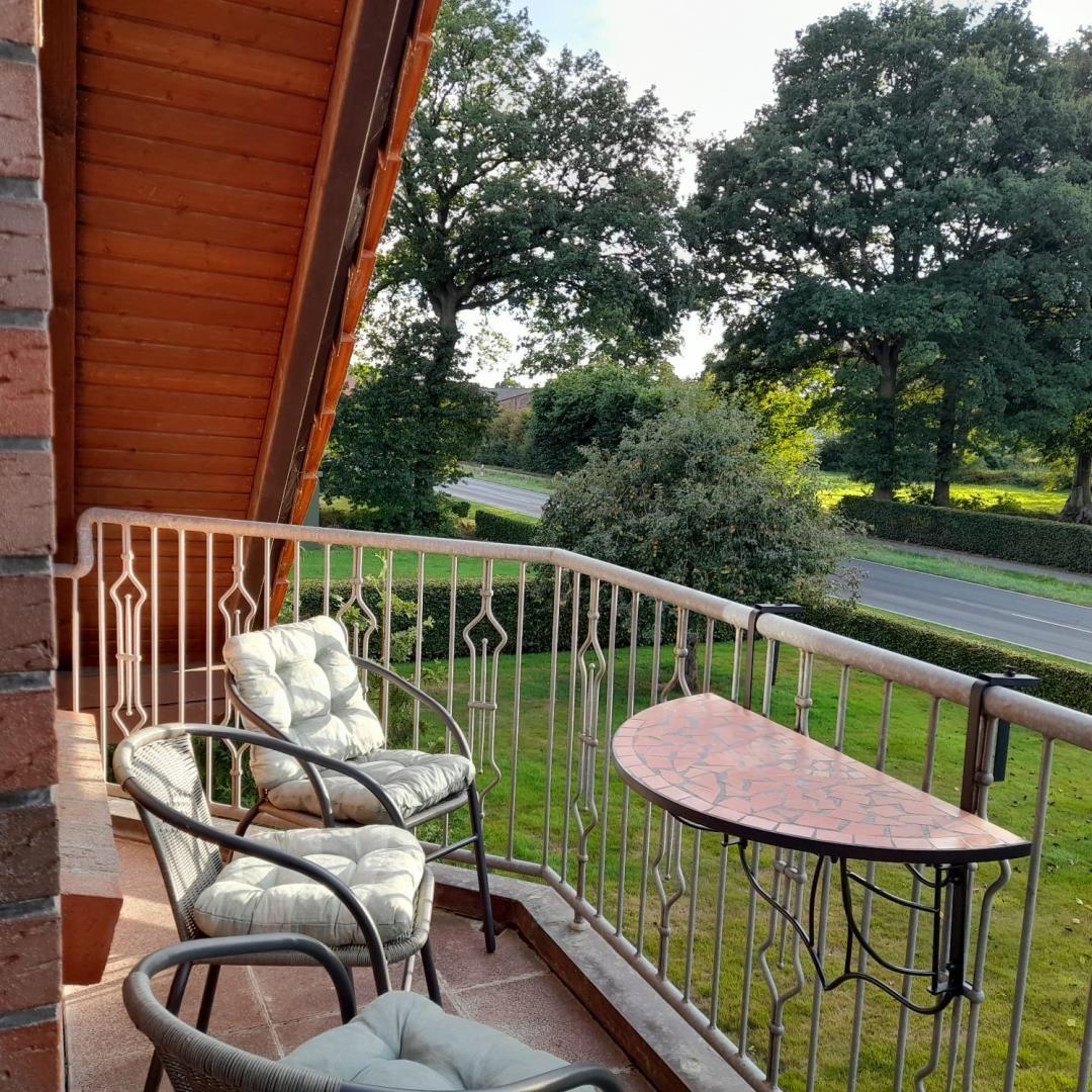 Balkon mit Sesseln, Sitzkissen und Mosaiktisch vor Rasen und Bäumen.
