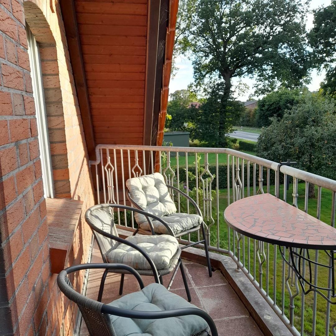 Balkon mit drei Korbstühlen, Mosaiktisch am Geländer und Blick auf Bäume.