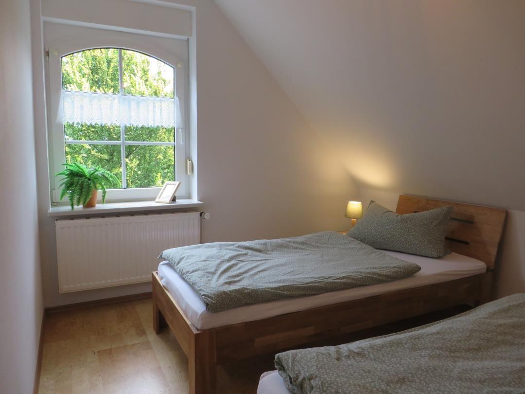 Schlafzimmer mit Holzbett, grüner Bettwäsche, Rundbogenfenster und Heizkörper.