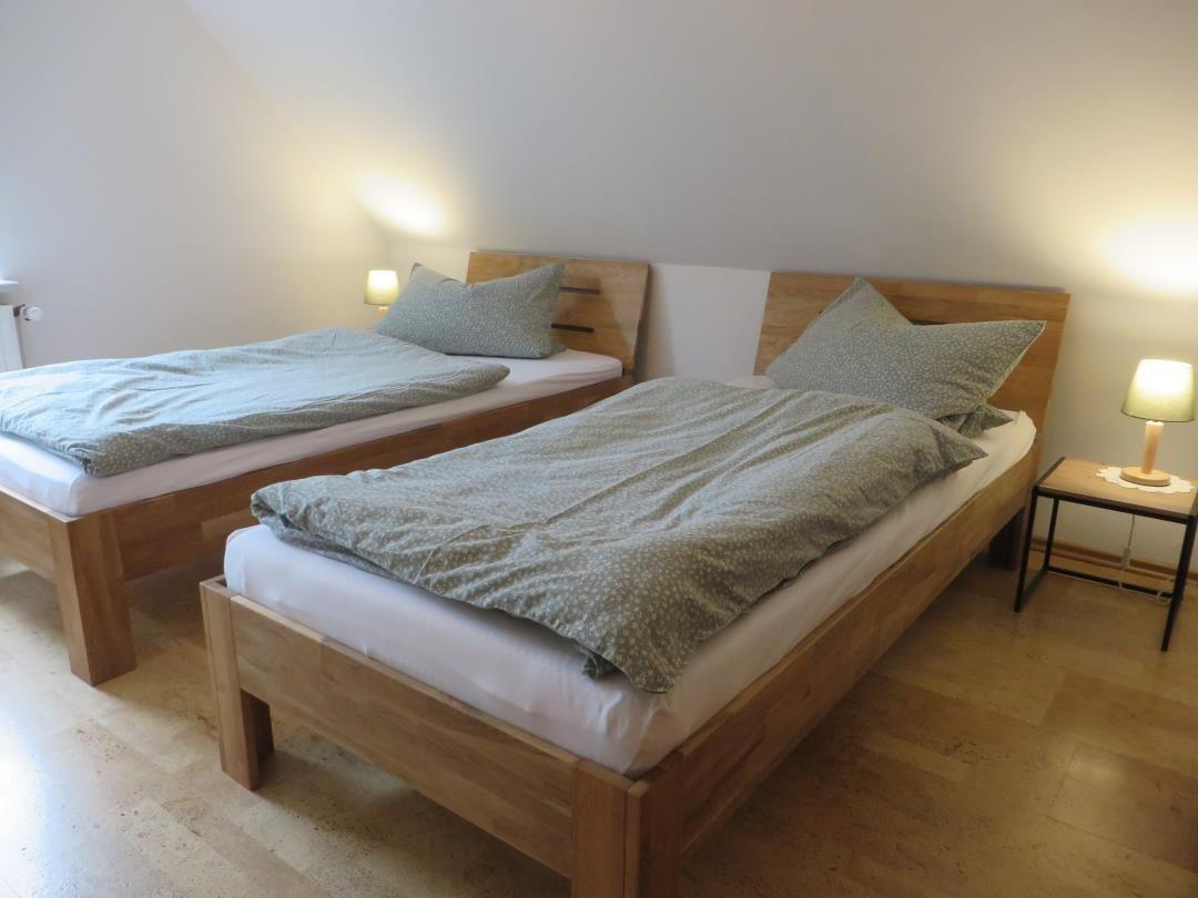 Zwei Holz-Einzelbetten mit grüner Bettwäsche und Nachttisch unter Dachschräge.