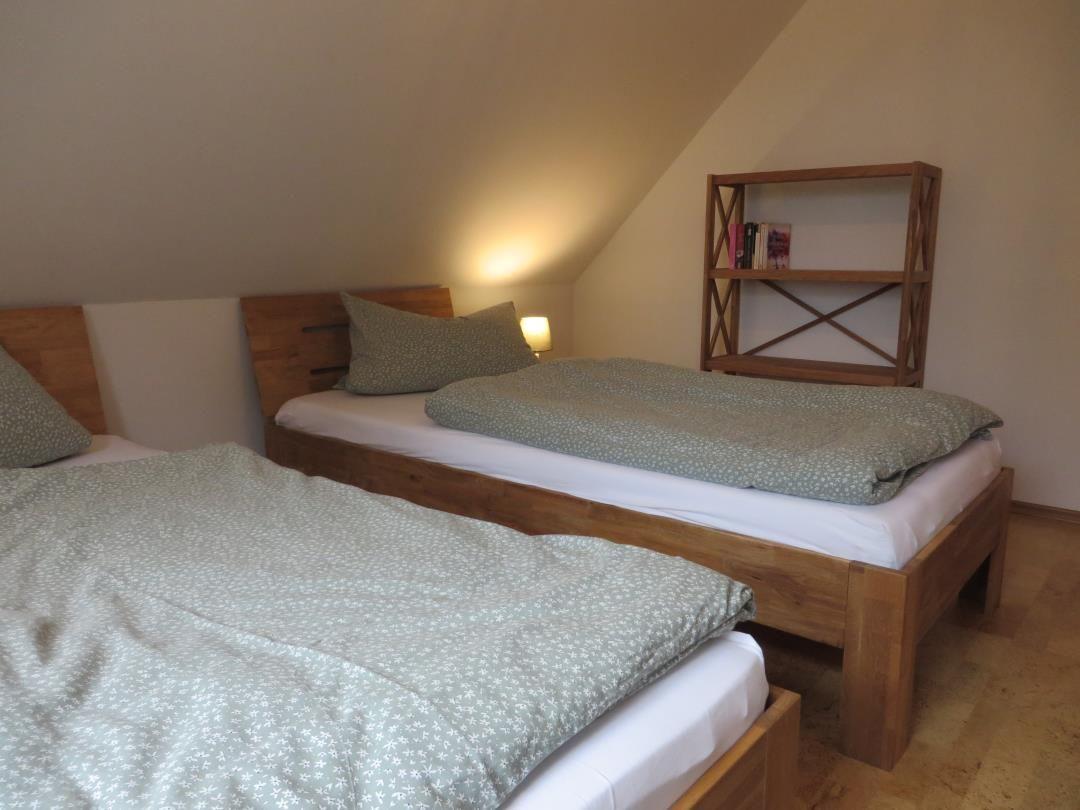 Zwei Holz-Einzelbetten mit grüner Bettwäsche und offenem Holzregal unter Dachschräge.