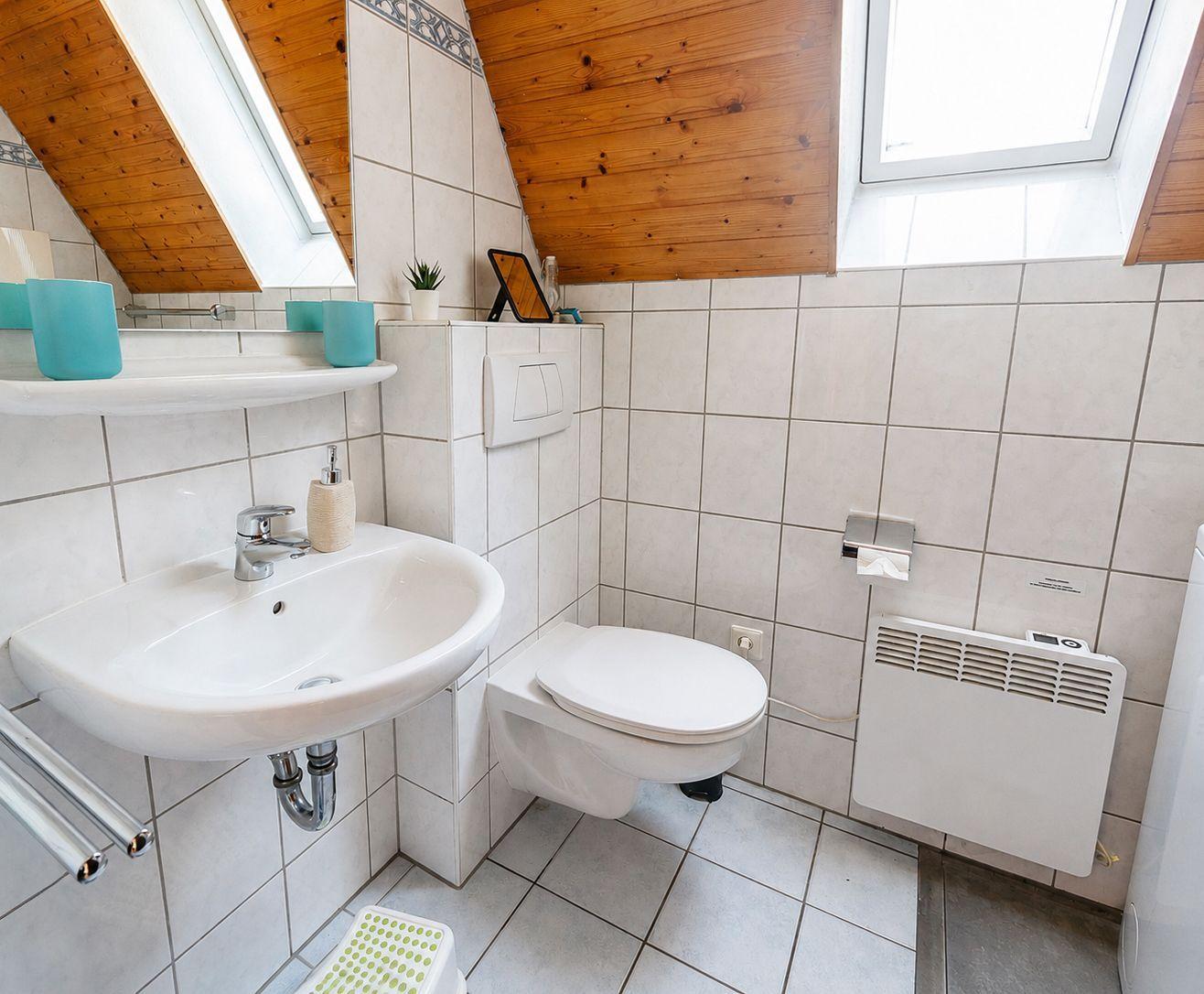 Badezimmer mit Waschbecken, WC, Dachfenster und schräger Holzdecke.