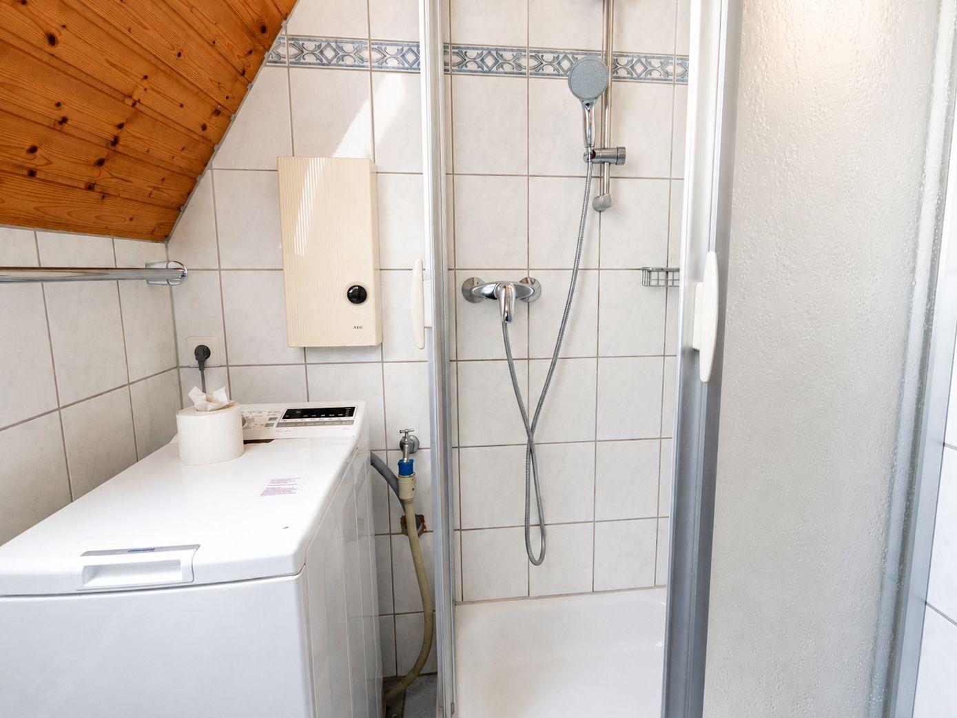 Badezimmer mit Toplader-Waschmaschine, Glasdusche und schräger Holzdecke.