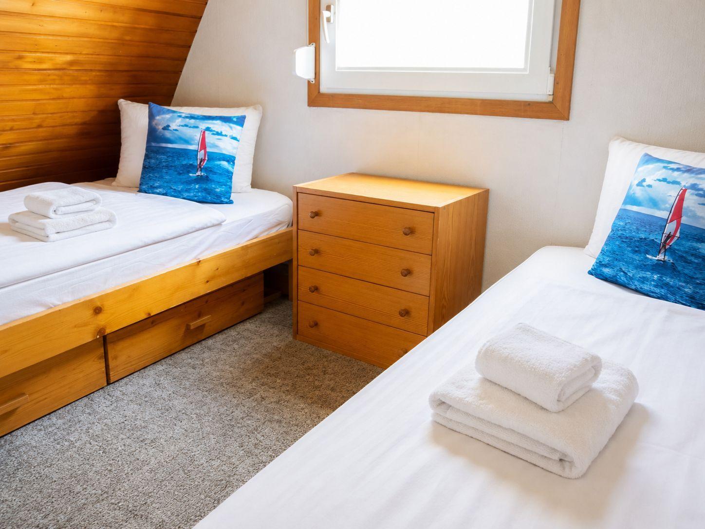 Schlafzimmer mit zwei Holz-Einzelbetten, Kommode dazwischen und Handtüchern.